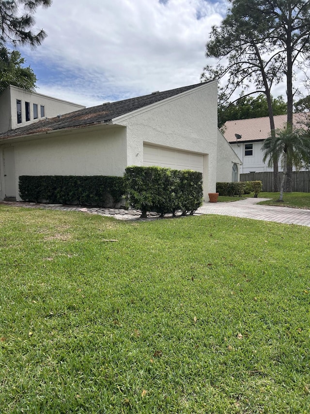 view of property exterior with an attached garage, a lawn, driveway, and stucco siding