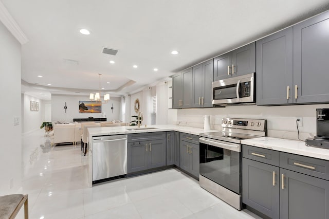 kitchen featuring a peninsula, appliances with stainless steel finishes, a sink, open floor plan, and gray cabinetry