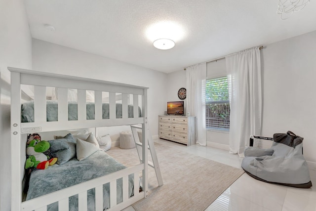 bedroom featuring baseboards, light tile patterned flooring, and a textured ceiling
