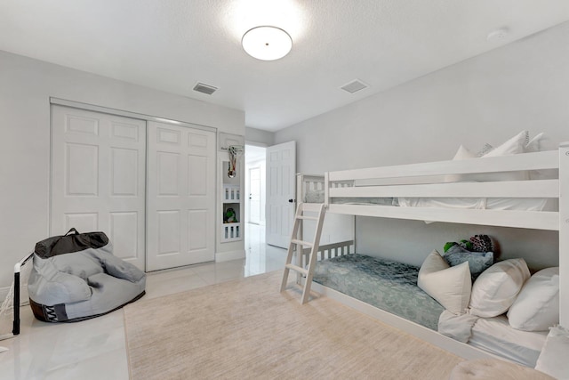tiled bedroom with a textured ceiling, a closet, and visible vents