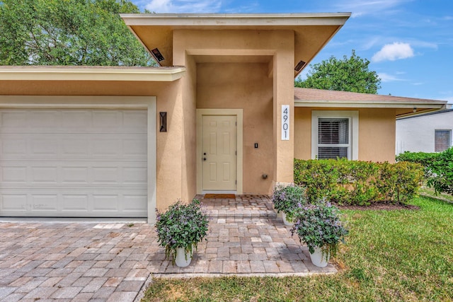 doorway to property with driveway, a garage, and stucco siding
