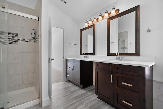 full bath with double vanity, vaulted ceiling, a shower stall, a sink, and wood finished floors