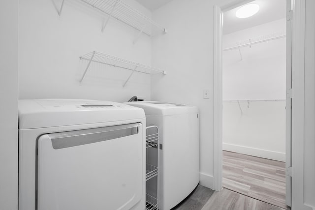 clothes washing area with baseboards, light wood finished floors, washing machine and dryer, and laundry area