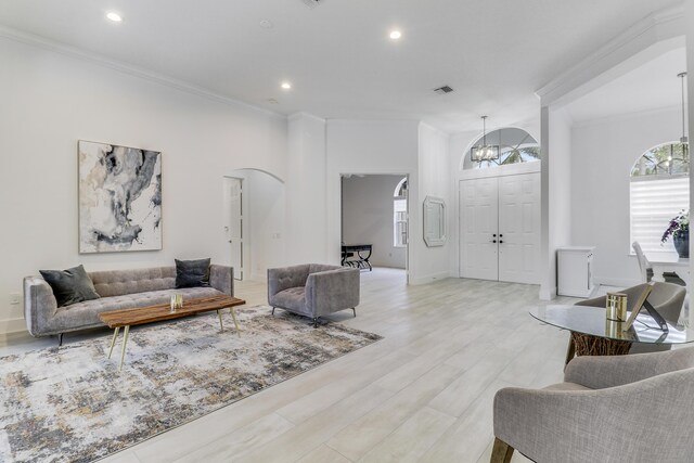 living room featuring arched walkways, light wood finished floors, crown molding, and visible vents