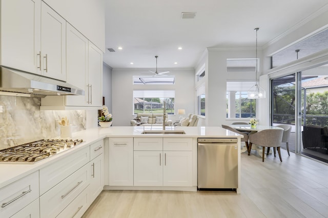 kitchen featuring crown molding, white cabinetry, under cabinet range hood, light countertops, and stainless steel appliances