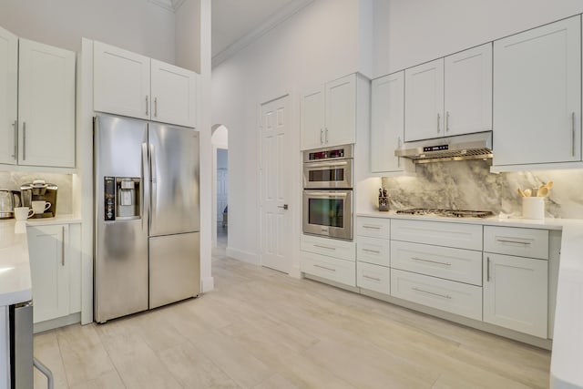 kitchen with tasteful backsplash, arched walkways, appliances with stainless steel finishes, under cabinet range hood, and light countertops