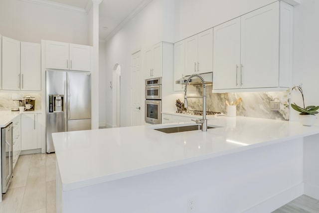 kitchen featuring tasteful backsplash, light countertops, a peninsula, crown molding, and stainless steel appliances