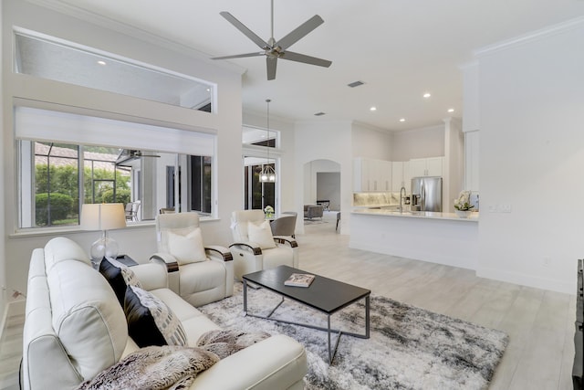 living room with arched walkways, light wood finished floors, ornamental molding, and ceiling fan