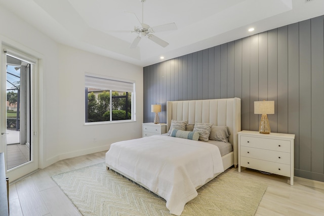 bedroom with baseboards, a raised ceiling, ceiling fan, light wood finished floors, and access to exterior