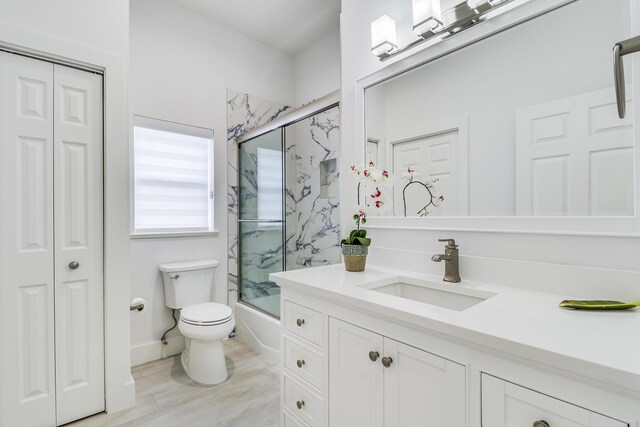 full bathroom with bath / shower combo with glass door, vanity, a closet, and toilet
