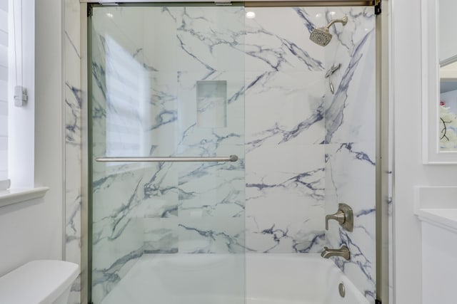 bathroom with toilet and shower / bath combination with glass door