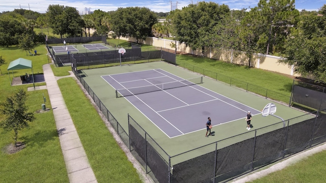 view of tennis court featuring fence, community basketball court, and a lawn