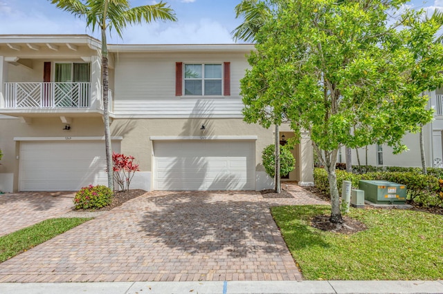 townhome / multi-family property featuring an attached garage, a balcony, stucco siding, and decorative driveway