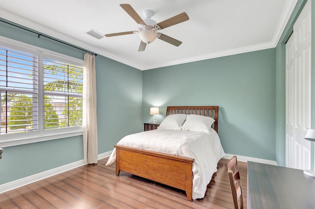 bedroom with baseboards, crown molding, a ceiling fan, visible vents, and wood finished floors