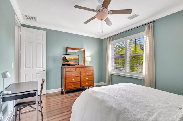 bedroom with visible vents, baseboards, crown molding, and wood finished floors