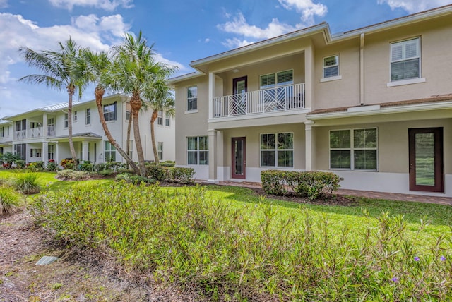 view of front of home with a front lawn, a balcony, and stucco siding