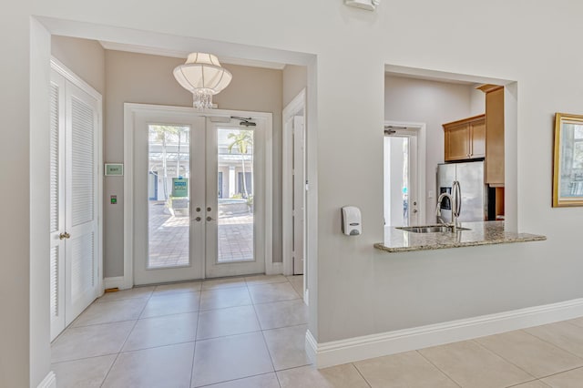 doorway with french doors, light tile patterned floors, a sink, and baseboards