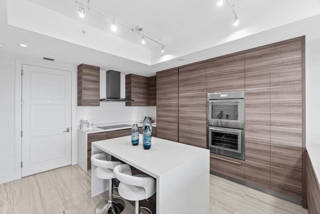 kitchen featuring rail lighting, wall chimney exhaust hood, a breakfast bar area, and modern cabinets