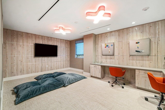 carpeted bedroom featuring built in study area, baseboards, and wooden walls