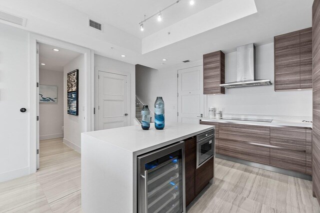 kitchen featuring wine cooler, light countertops, visible vents, wall chimney range hood, and modern cabinets