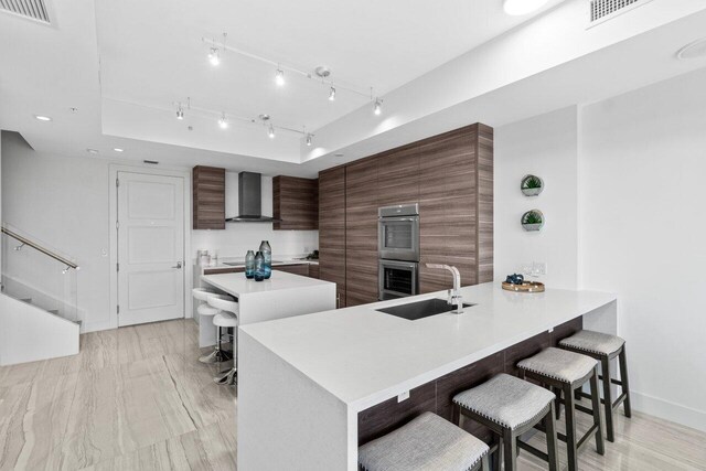 kitchen with a sink, modern cabinets, light countertops, wall chimney exhaust hood, and visible vents