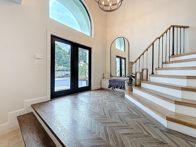 foyer entrance with stairs, a high ceiling, a notable chandelier, and french doors