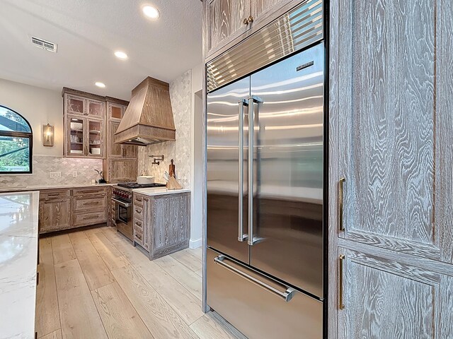 kitchen with high quality appliances, visible vents, premium range hood, light wood finished floors, and recessed lighting