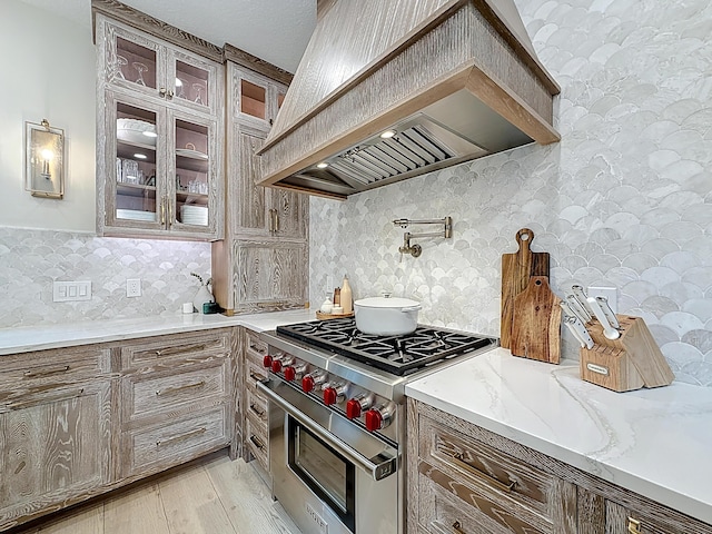 kitchen featuring custom exhaust hood, glass insert cabinets, designer range, and light wood-style floors