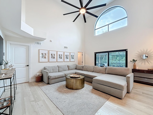 living room with visible vents, a ceiling fan, a towering ceiling, and light wood-type flooring