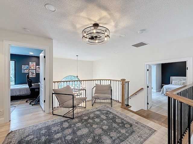 corridor featuring an inviting chandelier, light wood finished floors, a textured ceiling, and an upstairs landing