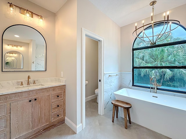 full bathroom featuring tile patterned flooring, vanity, toilet, a freestanding tub, and tile walls