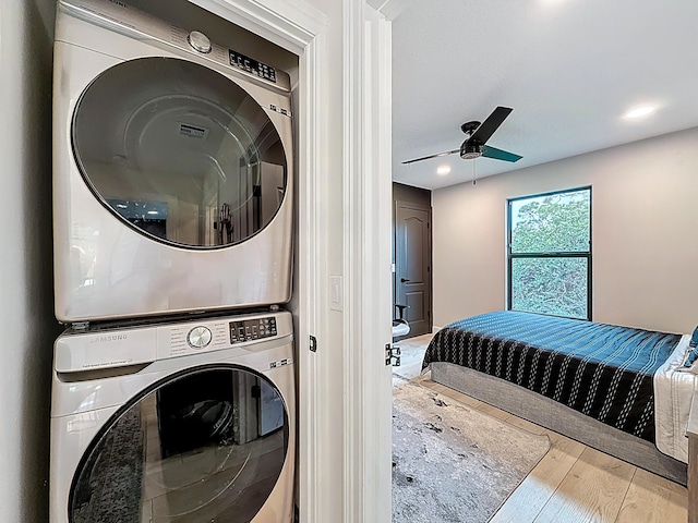 laundry room featuring wood finished floors, a ceiling fan, stacked washer / drying machine, and laundry area