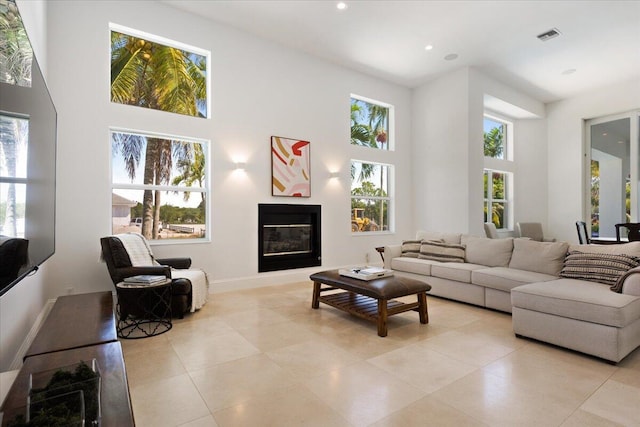 living area with visible vents, a glass covered fireplace, a towering ceiling, and light tile patterned floors