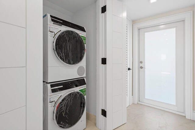 laundry area with stacked washer and clothes dryer, marble finish floor, and laundry area