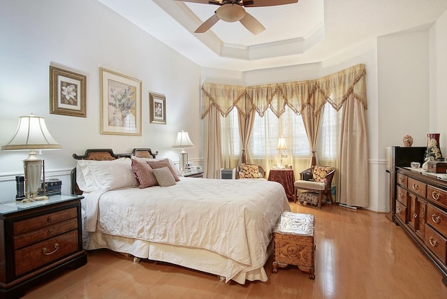 bedroom with a raised ceiling, light wood finished floors, ornamental molding, and ceiling fan
