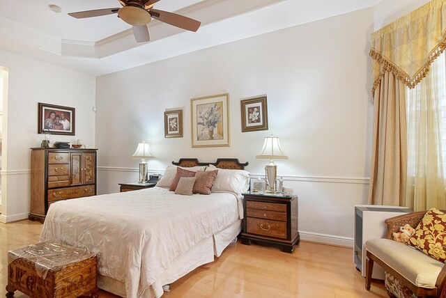 bedroom featuring light wood-style floors, a tray ceiling, baseboards, and ceiling fan