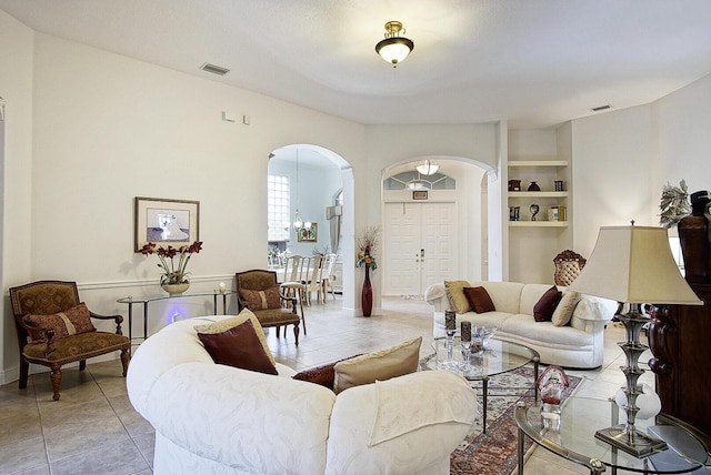 living room featuring arched walkways, light tile patterned flooring, and built in shelves