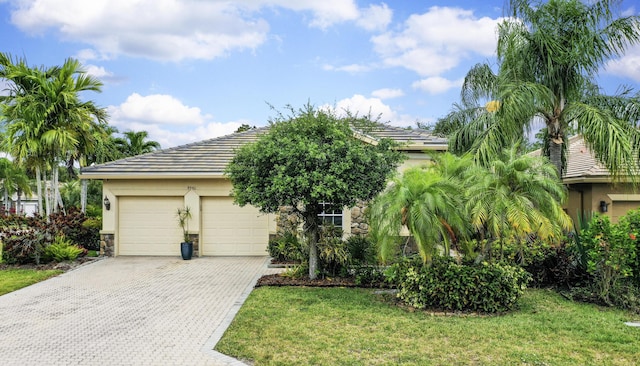 obstructed view of property featuring stucco siding, decorative driveway, an attached garage, a front lawn, and stone siding