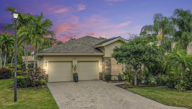 view of property hidden behind natural elements featuring stone siding, stucco siding, a garage, decorative driveway, and a tiled roof