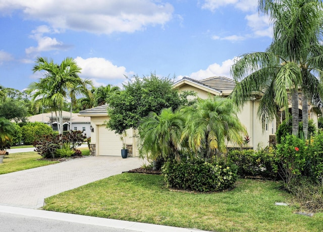 obstructed view of property with stucco siding, decorative driveway, a front yard, an attached garage, and a tiled roof