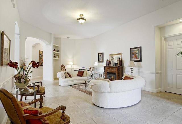 living area with light tile patterned flooring, built in features, and a glass covered fireplace