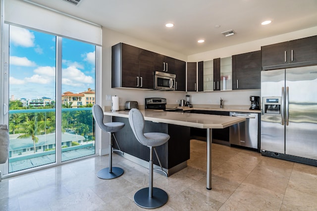 kitchen featuring a breakfast bar, stainless steel appliances, dark brown cabinets, light countertops, and recessed lighting