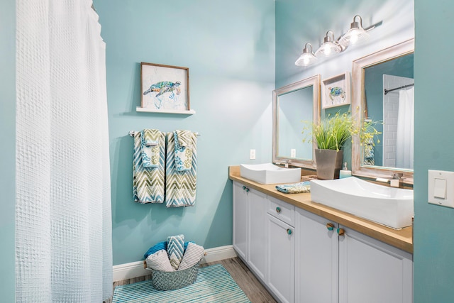 full bath featuring a sink, baseboards, double vanity, and wood finished floors