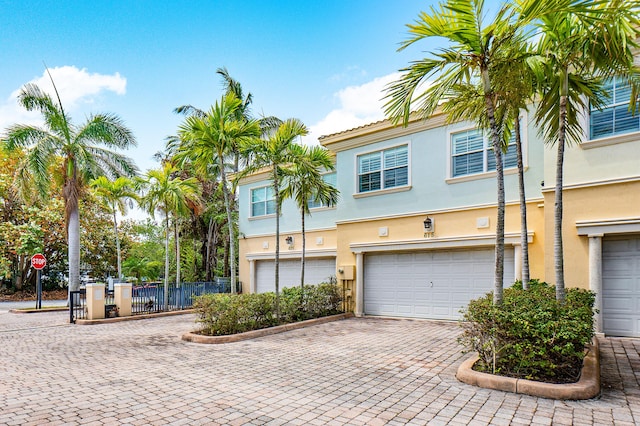 townhome / multi-family property with a garage, decorative driveway, stucco siding, and fence