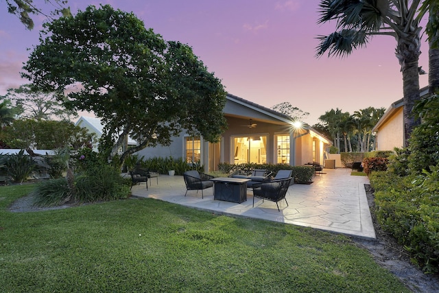 13810 Crosspointe Ct, Palm Beach Gardens, FL 33418 - back of house at dusk with a patio, a fire pit, stucco siding, ceiling fan, and a yard