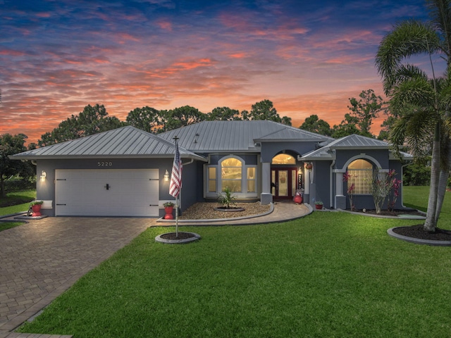 single story home featuring stucco siding, decorative driveway, metal roof, a front lawn, and a garage