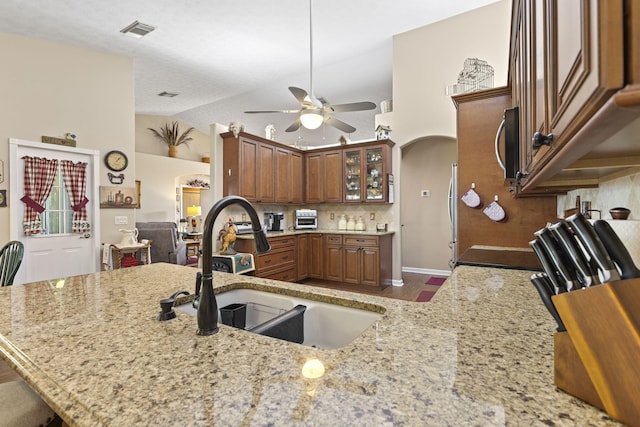 kitchen with a ceiling fan, visible vents, light stone counters, stainless steel microwave, and a sink