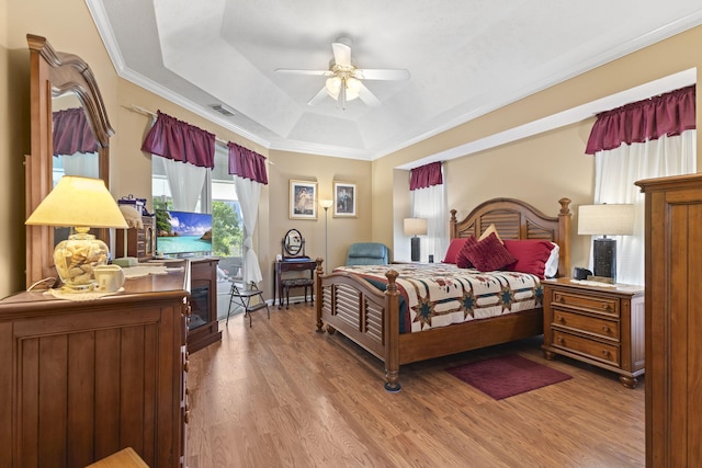 bedroom featuring crown molding, ceiling fan, visible vents, wood finished floors, and a raised ceiling
