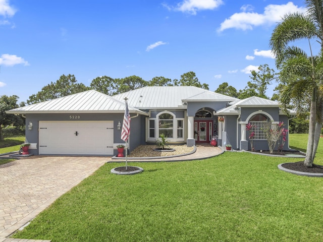 ranch-style house featuring a garage, a front yard, stucco siding, and decorative driveway