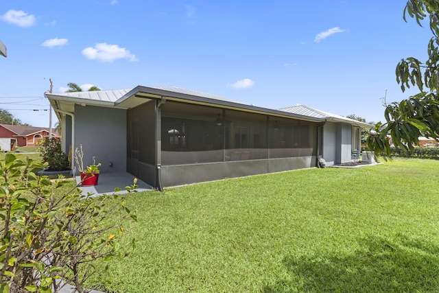 rear view of house with a yard, metal roof, a sunroom, and stucco siding